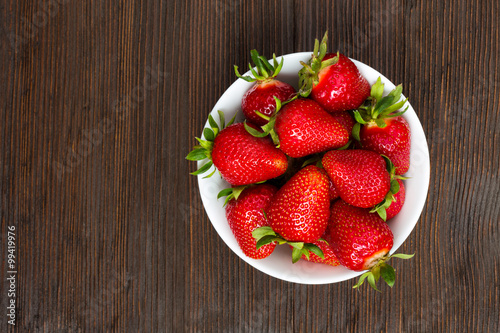 Fresh ripe strawberries in a simple white bowl, on dark wooden table