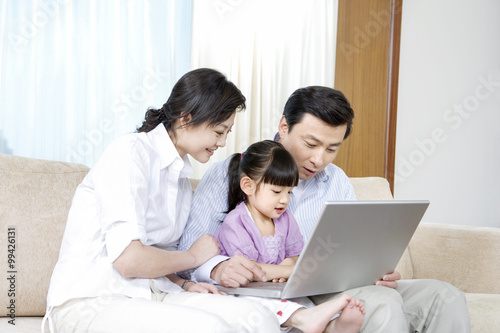 Young couple and daughter look at laptop on sofa