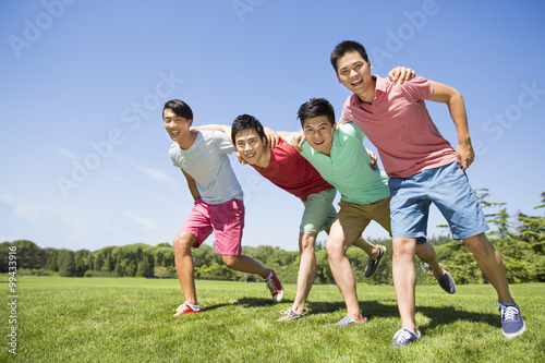 Four cheerful young men standing arm in arm on grass
