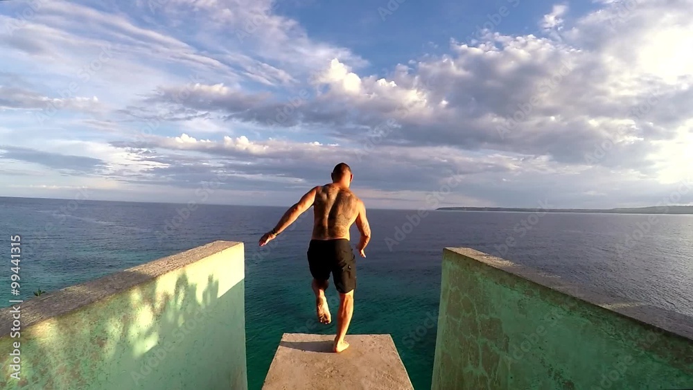 Jumping from cliff to the sea in Philippines on Siqiujor island. Tattoed man is running and jumping down.