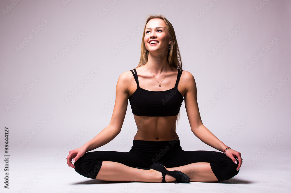 Fototapeta premium Nice Young woman doing gymnastic exercise with crossed legs on grey isolated background