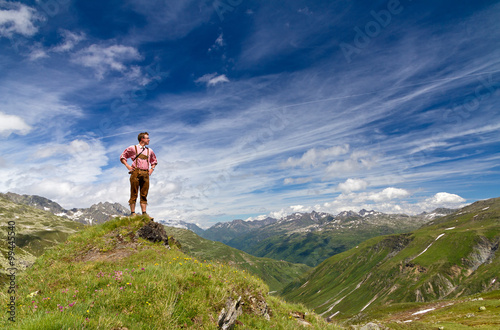 Young explorer in traditional clothing stands proud on top of a mountain in the Swiss Alps on a sunny summer day