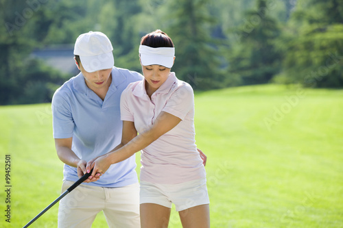 Young man teaching his girlfriend how to play golf