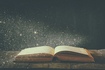 abstract image of open antique book on wooden table. selective focus. retro filtered and toned with glitter overlay

