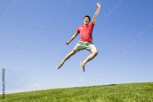 Cheerful young man jumping on grass