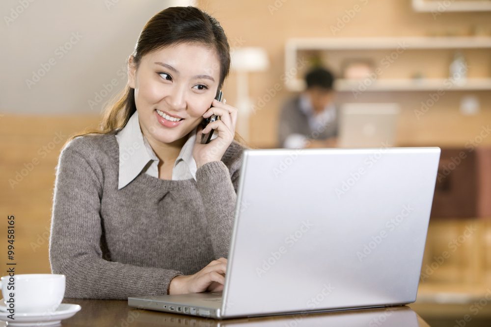 Young woman using mobile phone while on laptop Young woman using mobile phone while on laptop