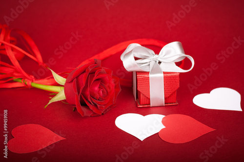 Rose, gift box and paper hearts on intense red background. Matte background. White elements.