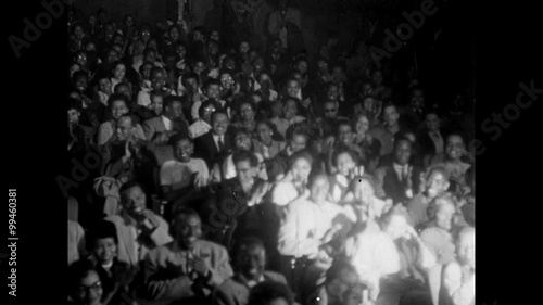 Audience applauding in theater as spotlight pans from left to right , 1950s