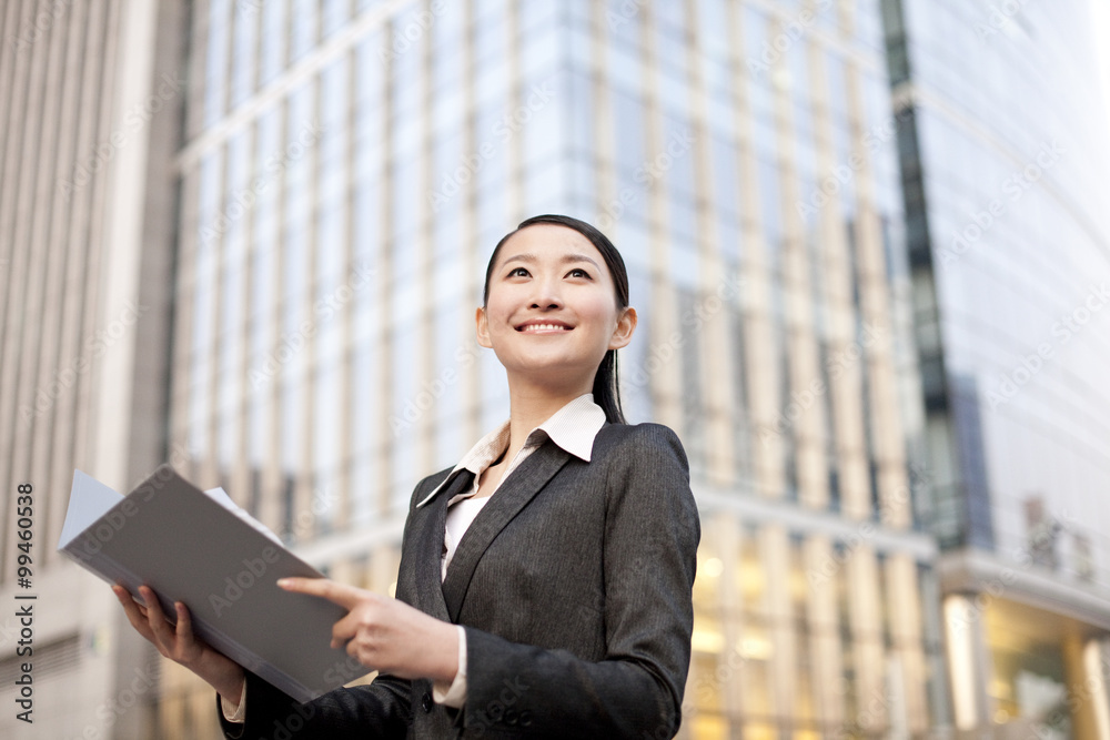 A businesswoman with a file folder outside office buildings contemplating A businesswoman with a file folder outside office buildings contemplating