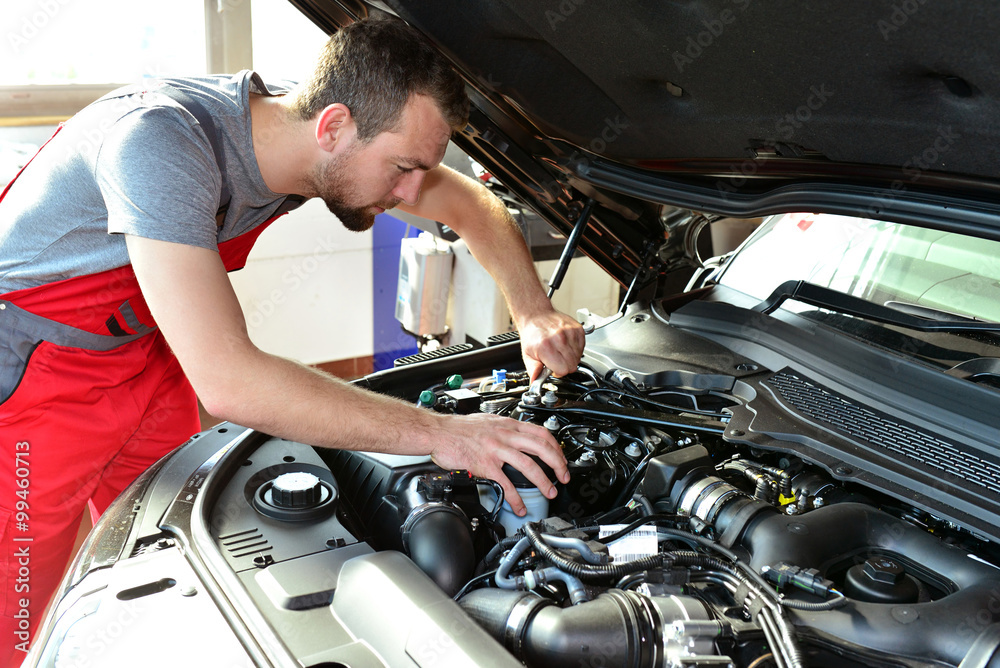 KFZ Mechaniker repariert Motor eines Fahrzeugs in der Autowerkstatt // Car mechanic repairs engine of a vehicle in the garage