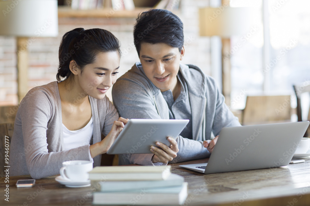 Young couple using laptop and digital tablet in cafe Young couple using laptop and digital tablet in cafe