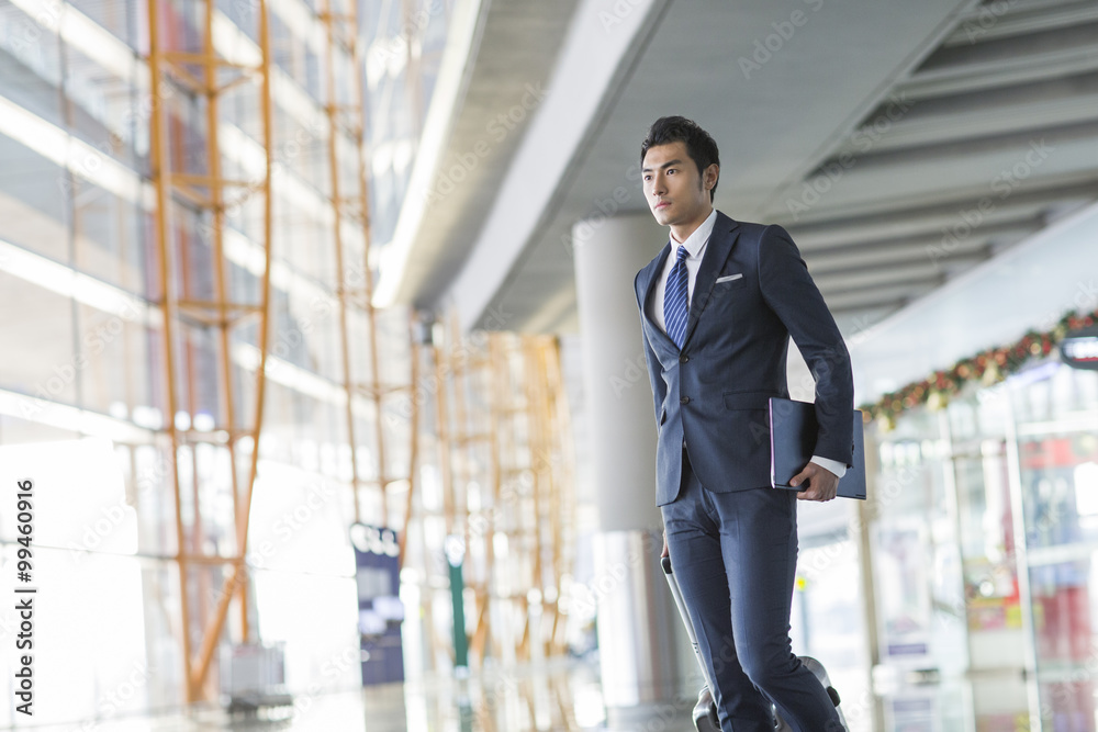 Young businessman walking in airport with suitcase and laptop
