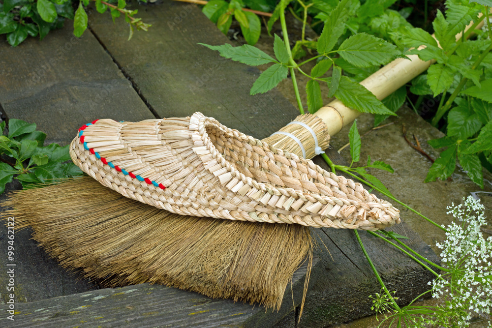плетеный тапок и метла с бамбуковой ручкой лежат в саду Stock-Foto ...