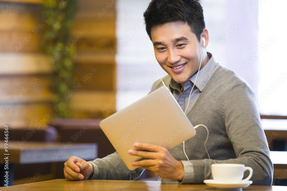Young man enjoying videos in digital tablet in coffee shop Young man enjoying videos in digital tablet in coffee shop