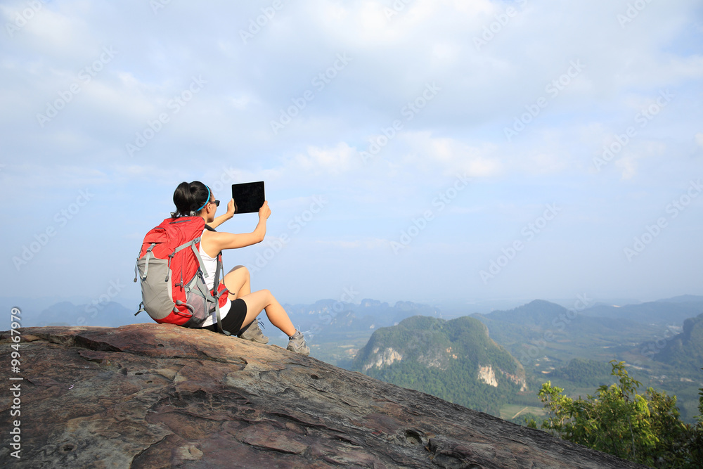 Obraz premium young woman hiker taking photo with digital tablet on mountain peak