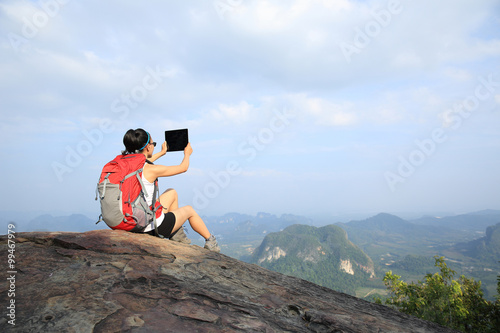 young woman hiker taking photo with digital tablet on mountain peak
