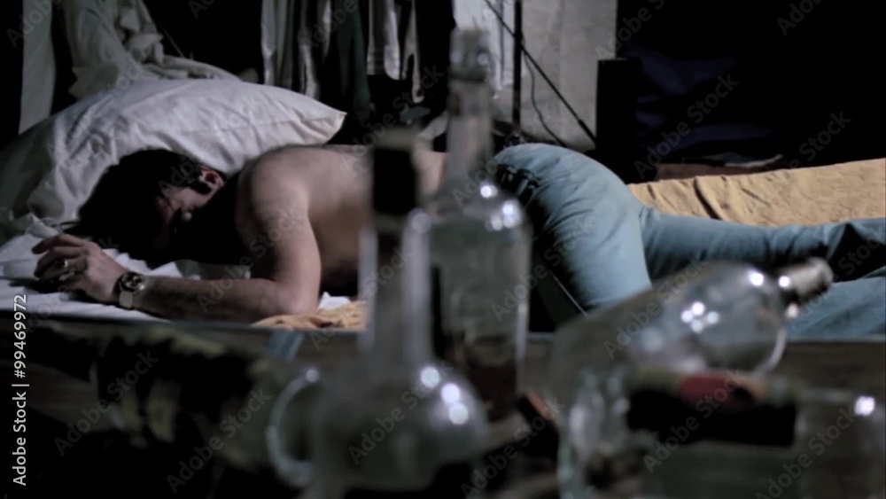 Empty liquor bottles on table with man sleeping in background 