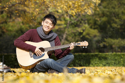 Male college student with guitar and books enjoying the pleasant weather in the autumn