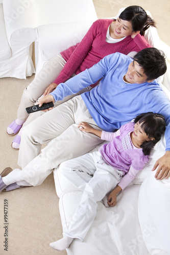 Young Chinese family sitting on a sofa watching television