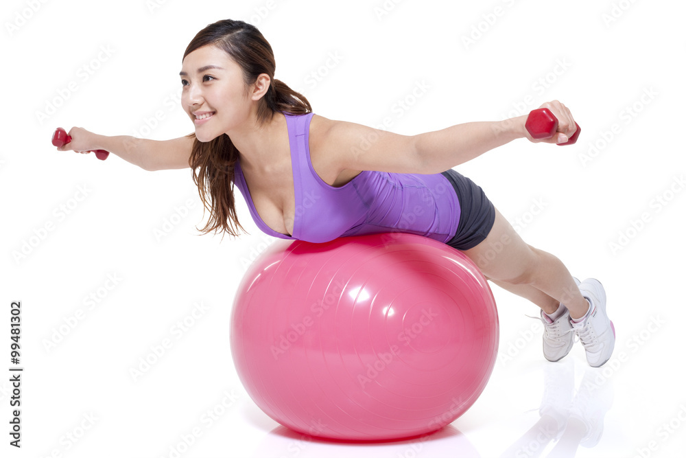 Young woman balancing on a fitness ball with dumbbells Young woman balancing on a fitness ball with dumbbells