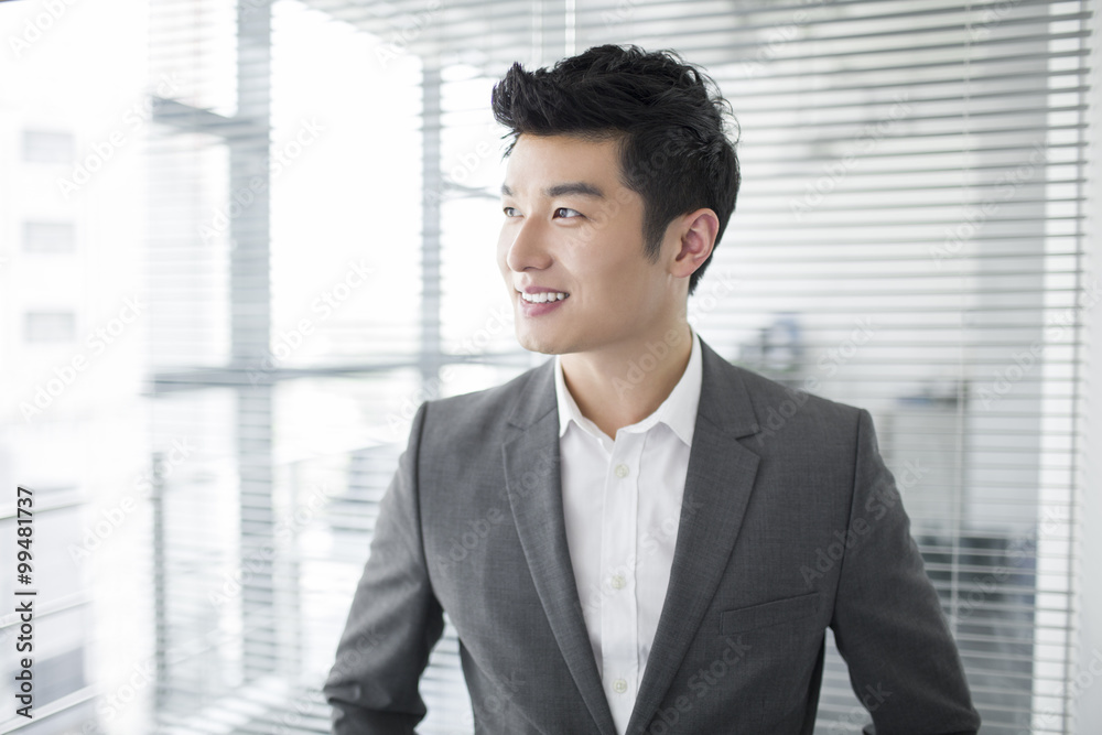Young businessman looking through window in office Young businessman looking through window in office