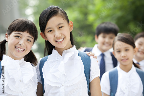 Happy schoolgirls in uniform with friends outdoors