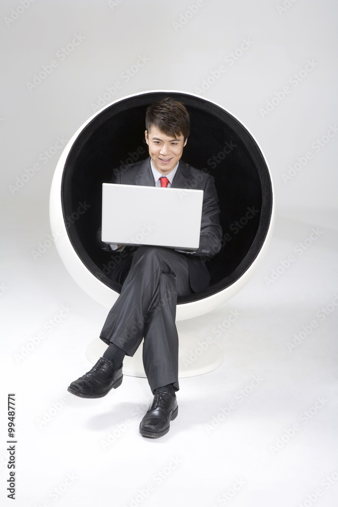 Young businessman using a laptop in a ball chair Young businessman using a laptop in a ball chair