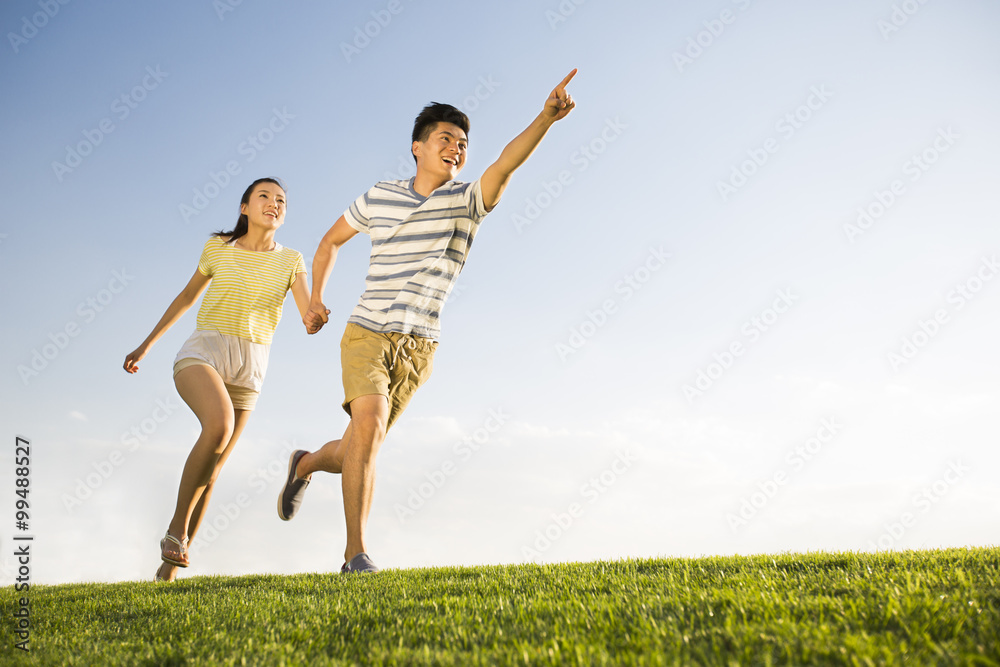 Cheerful young couple holding hands running on grass