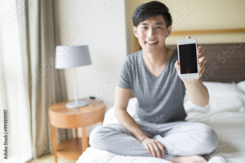 Young man showing smart phone on bed