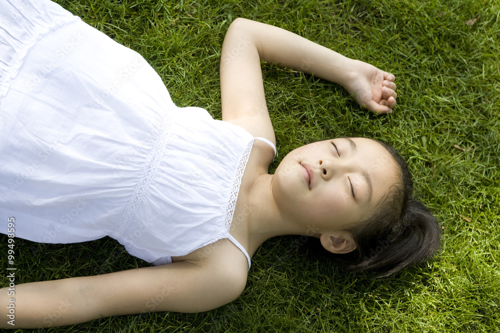 Little girl in white dress playing lying on the grass