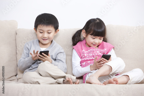 Excited boy and girl playing smart phone in sofa
