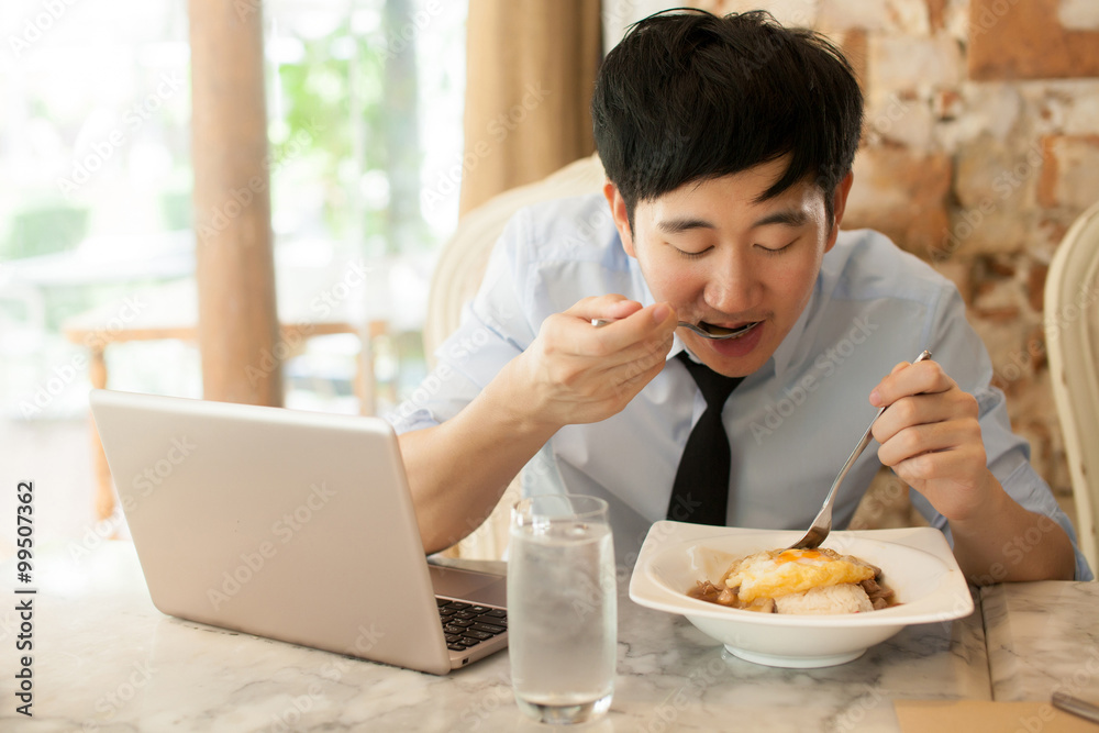 Young Asian man working while eating with his laptop in restaurant Young Asian man working while eating with his laptop in restaurant