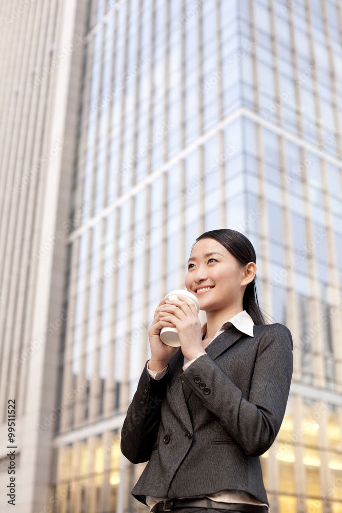 A businesswoman with a cup of coffee outside office buildings contemplating A businesswoman with a cup of coffee outside office buildings contemplating