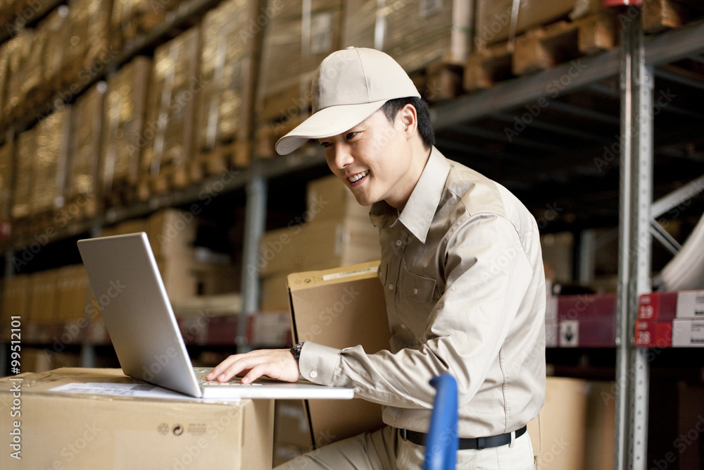 Male Chinese warehouse worker using a laptop Male Chinese warehouse worker using a laptop