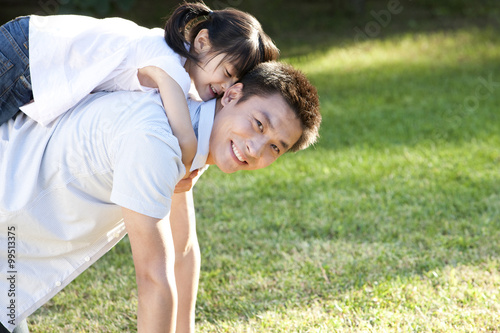 Young Chinese father with daughter on piggyback outdoors