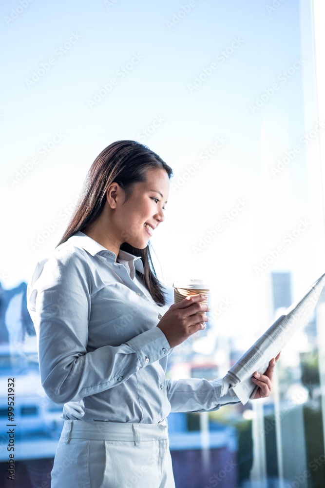 Smiling businesswoman holding disposable cup reading newspaper