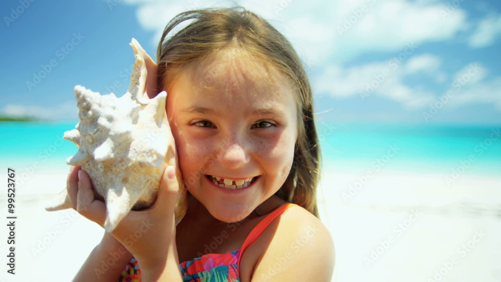 Portrait of cute smiling Caucasian girl on tropical beach holding conch shell