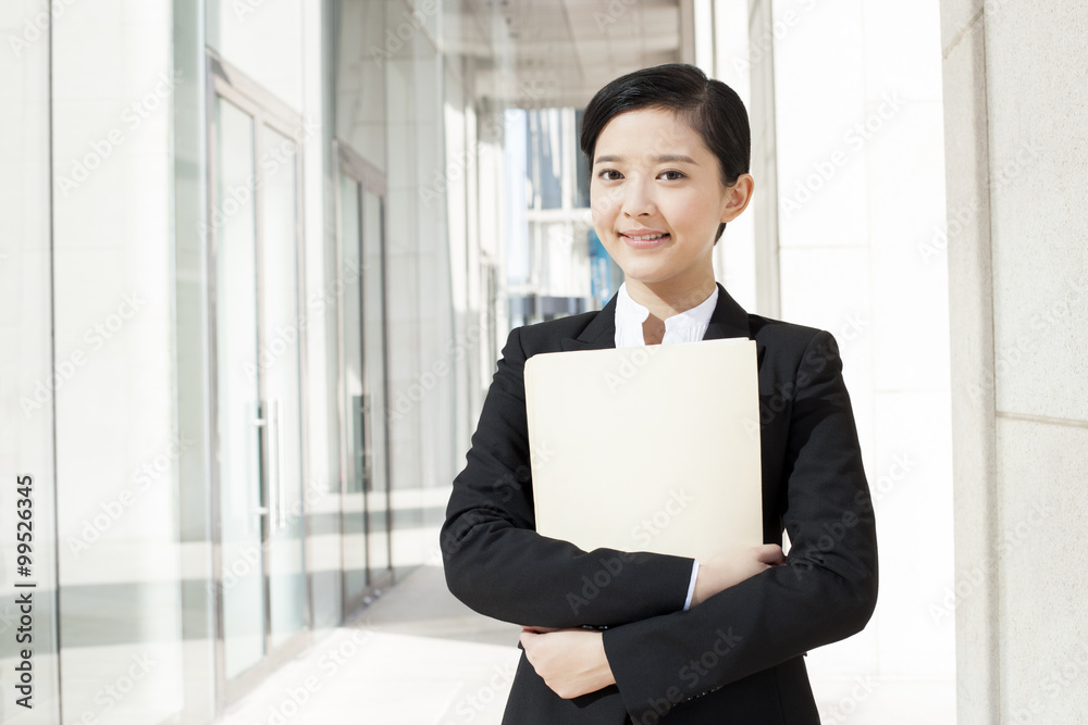 Smiling young businesswoman with a folder in downtown district Smiling young businesswoman with a folder in downtown district