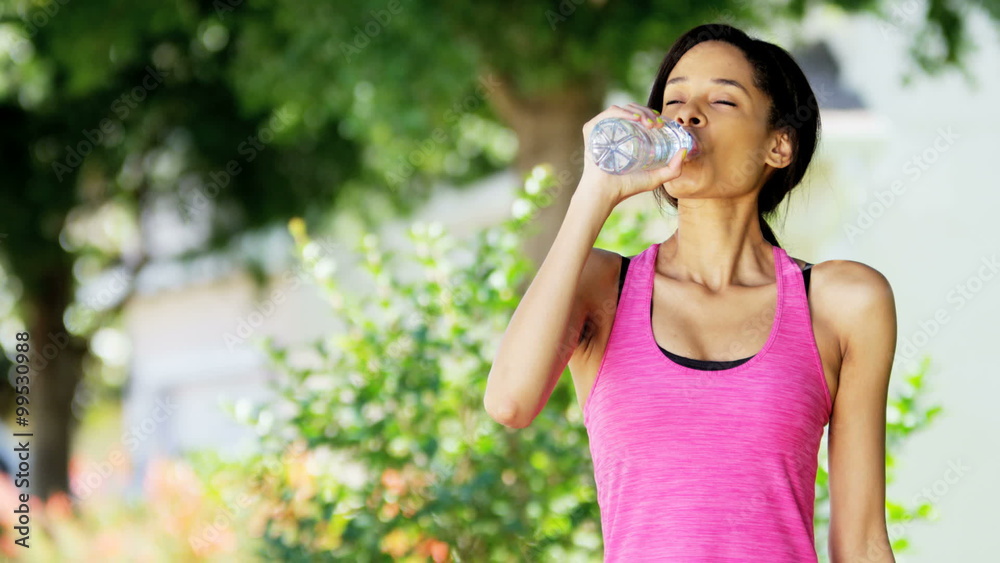 Young African American female drinking water and doing fitness routine outdoors Young African American female drinking water and doing fitness routine outdoors