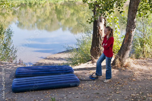 Rest at nature. Girl pumps up an inflatable mattress