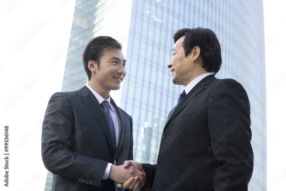 Businessmen shaking hands in front of tall building Businessmen shaking hands in front of tall building