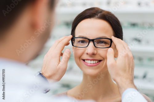 Fototapeta Naklejka Na Ścianę i Meble -  optician putting glasses to woman at optics store
