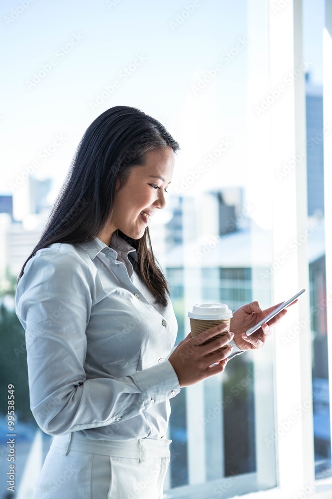 Smiling businesswoman using smartphone and holding hot drink
