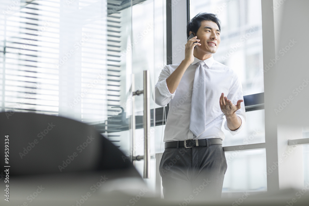 Young businessman talking on cell phone in office Young businessman talking on cell phone in office