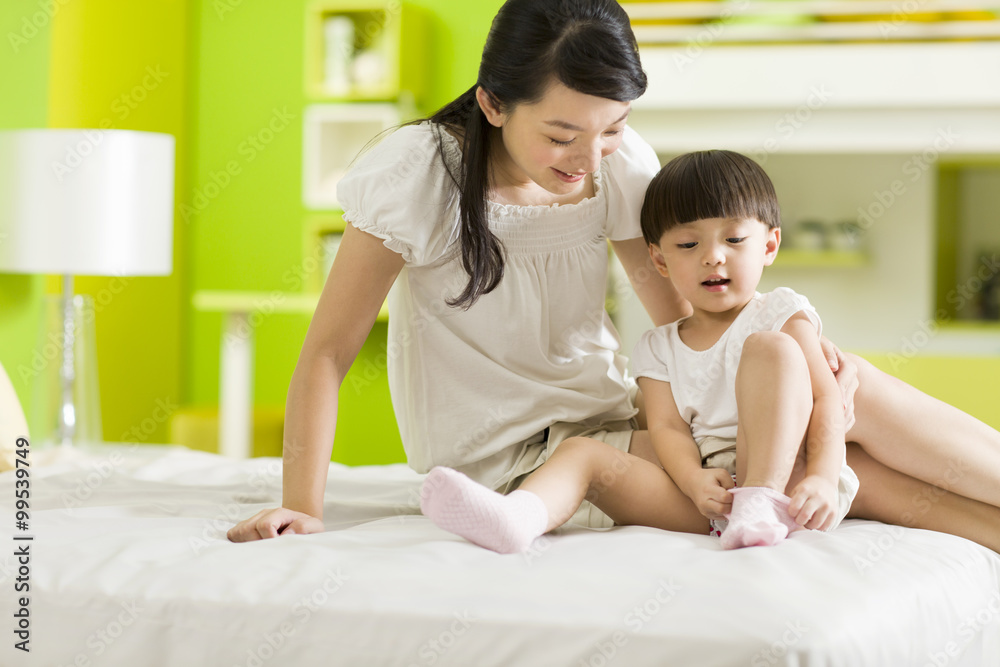 Mother watching young daughter putting her socks on Mother watching young daughter putting her socks on