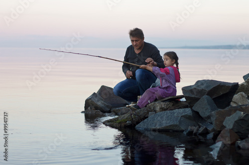 Father and daughter fishing at sunset on lake