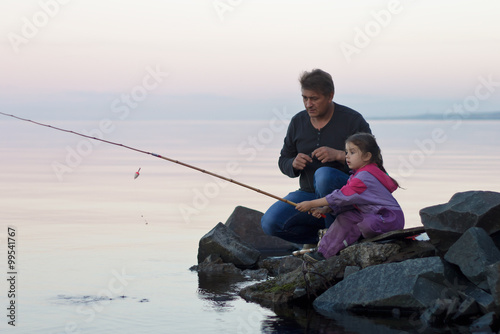 Father and daughter fishing at sumer sunset on lake