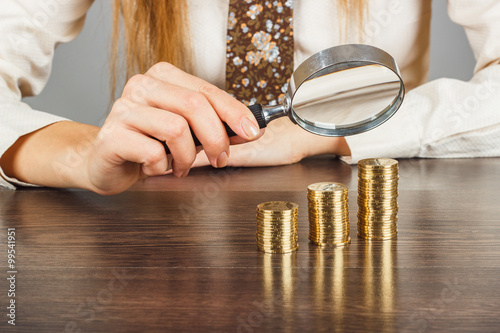Woman's hands with magnifier and stacks of coins
