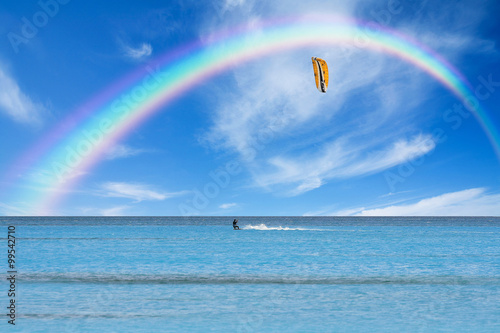 Kitesurfer in action on clear blue water under a rainbow