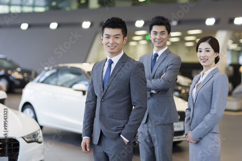 Confident salespeople standing with new cars in showroom © Blue Jean Images